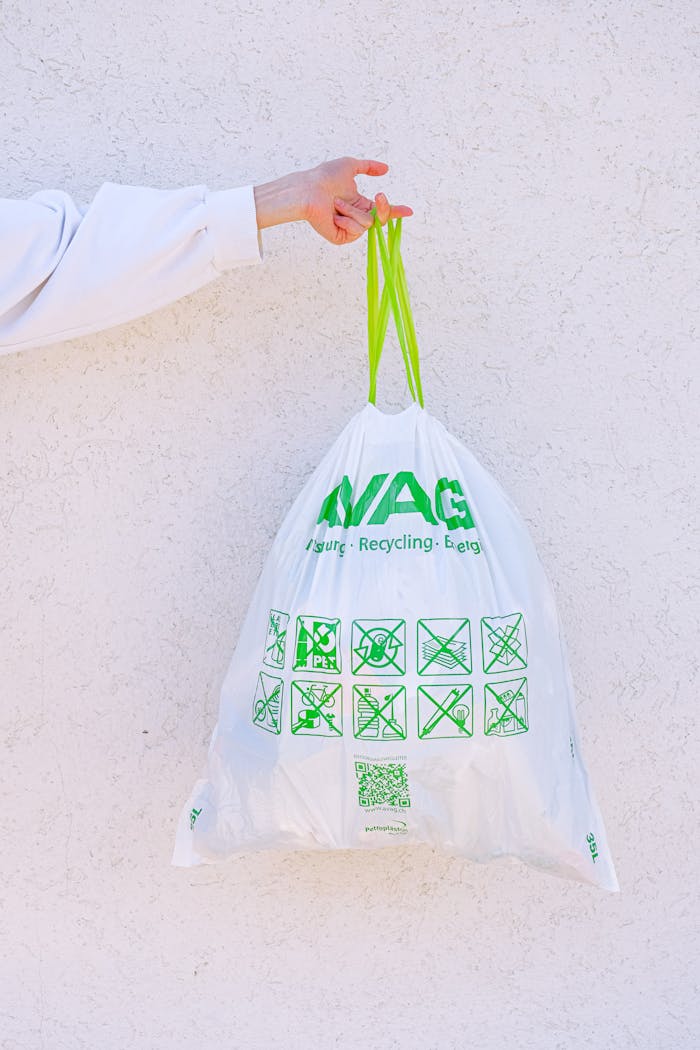 services-03 A person holding a white recycling bag with green symbols against a white wall, promoting sustainability.